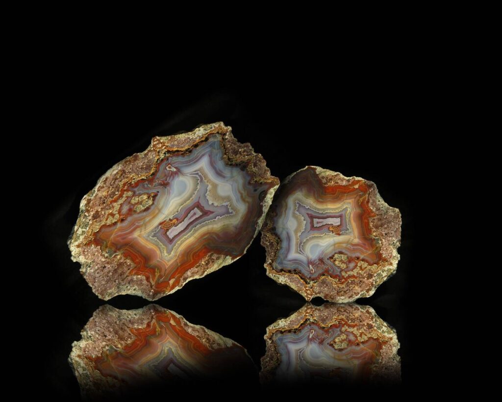 Aufgeschnittene Achat-Geode mit farbigen Bänderungen in Rot, Orange und Blaugrau auf schwarzem Hintergrund