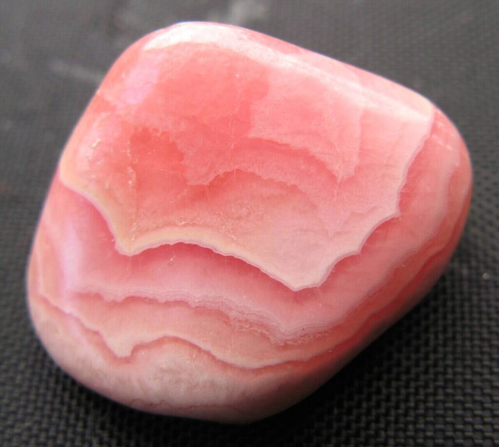 Polierter Rhodochrosit Trommelstein mit rosa-weißer Bänderung auf dunklem Hintergrund