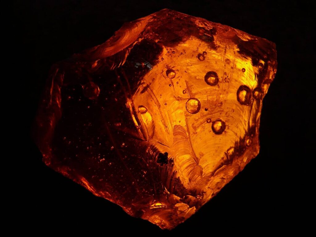 Bernstein im Durchlicht mit goldener Honigfarbe und eingeschlossenen Luftblasen auf schwarzem Hintergrund